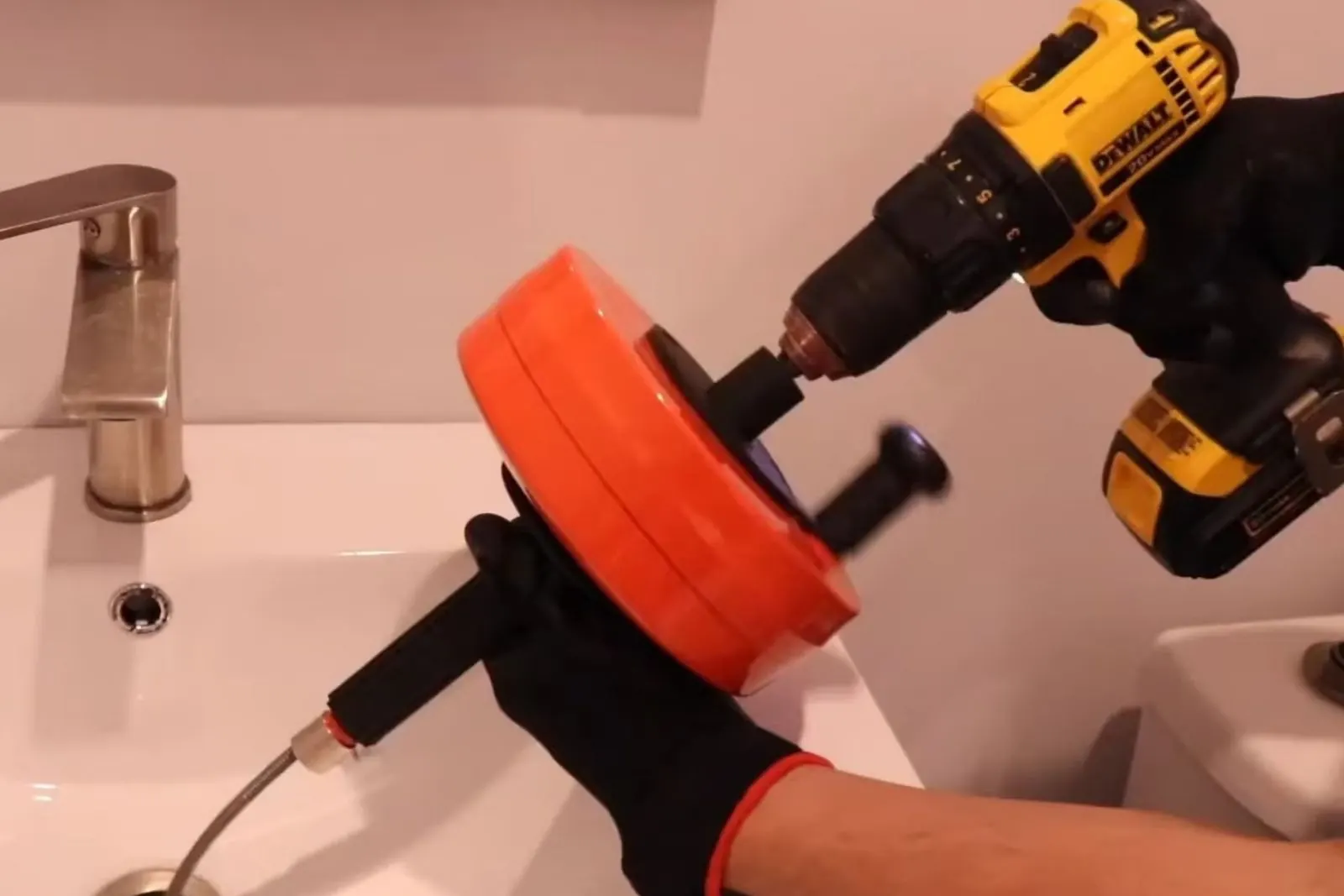 Plumber feeding a drill-powered drain auger into a bathroom sink drain