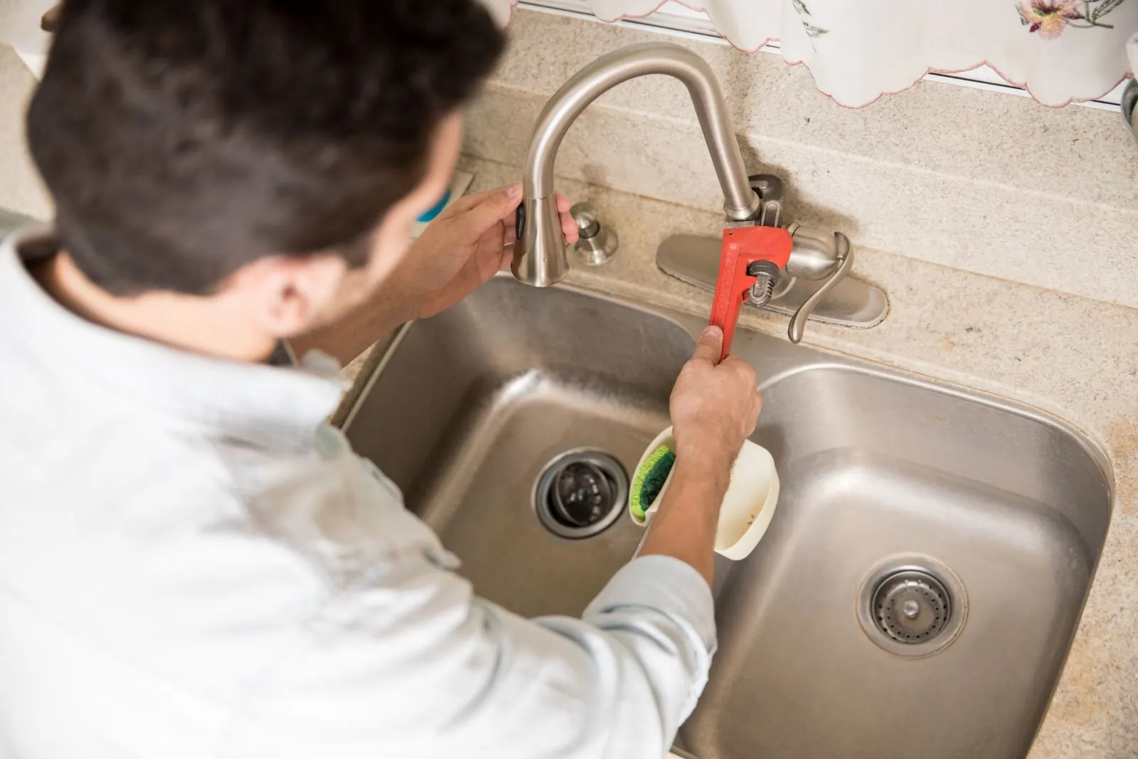 Plumber tightening a kitchen faucet connection over a stainless double sink