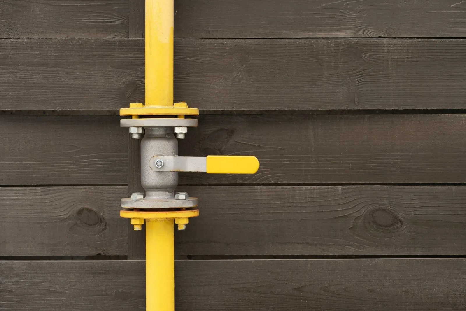 Yellow gas pipe with a quarter-turn shutoff valve mounted on an exterior wall