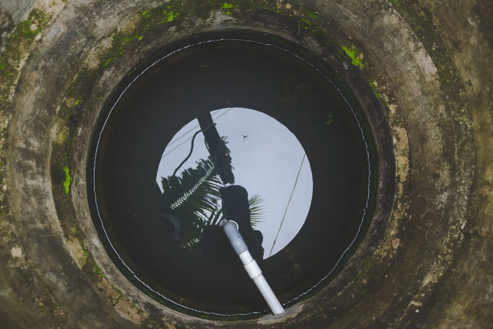 View up through a round underground sewer access shaft with a pipe entering from the side