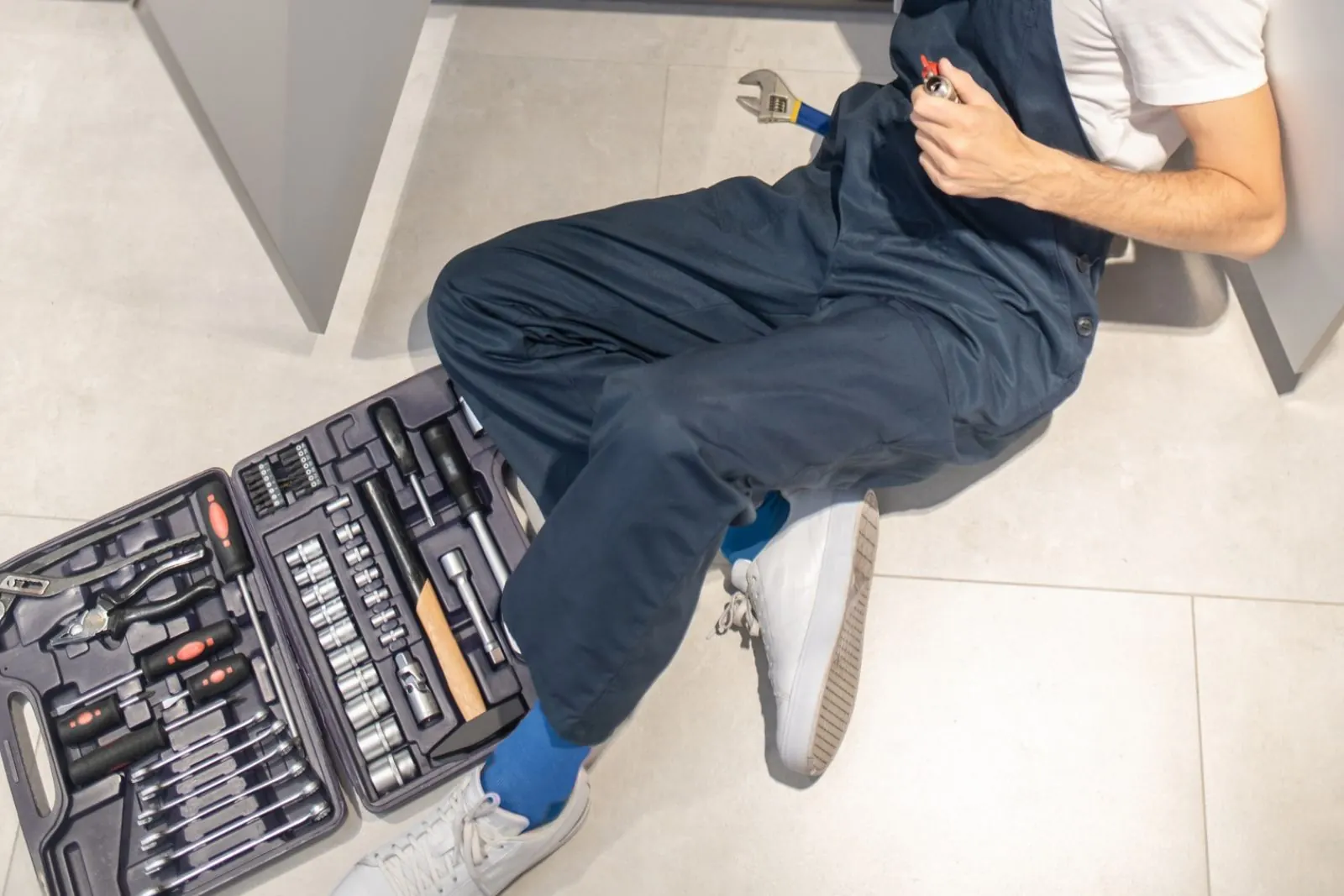 Technician lying under a fixture with an open tool case during a service call