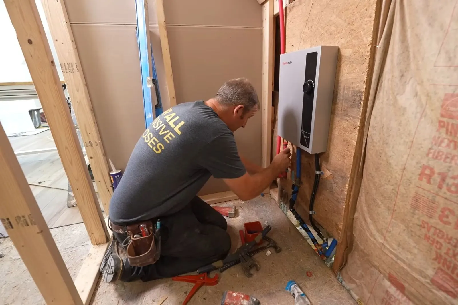 Plumber installing a wall-mounted tankless water heater in a framed wall